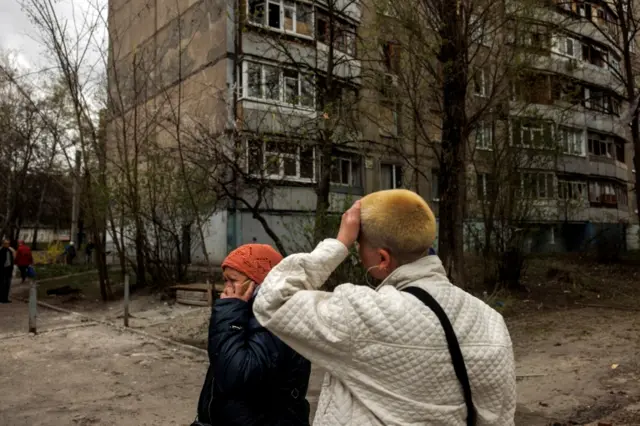 A woman reacts as another speaks on the phone in Kharkiv