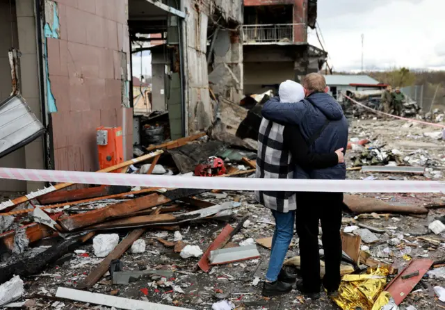 People hug as they look on at the destruction caused when a civilian building was hit by a Russian missile on April 18, 2022 in Lviv, Ukraine