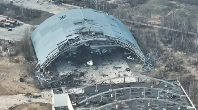 Image shows drone footage of damage to hangar and damaged aircraft