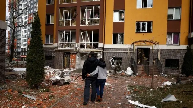 Civilians seen standing in front of a damaged building in Irpin