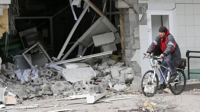 A man rides a bicycle near a damaged branch of PrivatBank in Mariupol