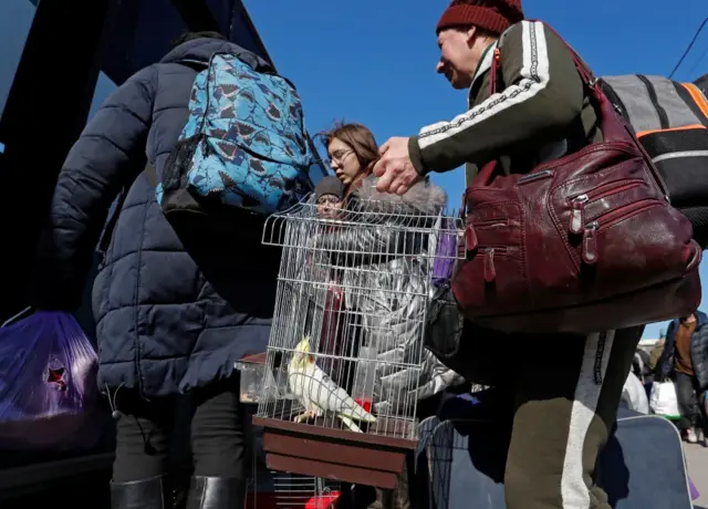 Evacuees, including a woman with a caged bird, board a bus to leave Mariupol