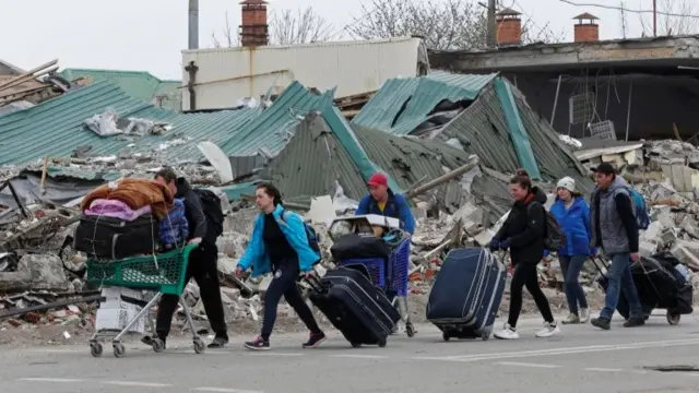 Local residents carry belongings past a building destroyed during Ukraine-Russia conflict in the southern port city of Mariupol,