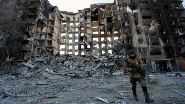 Pro-Russian troops soldier walks near an apartment building destroyed in the besieged southern port city of Mariupol