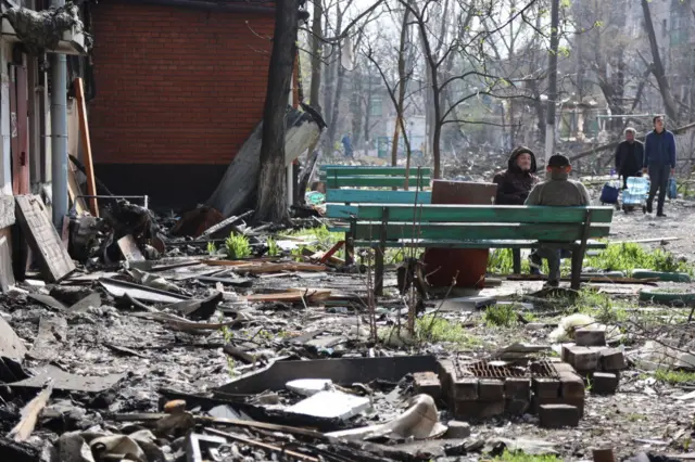 Residents sit on benches amid ruins in Mariupol