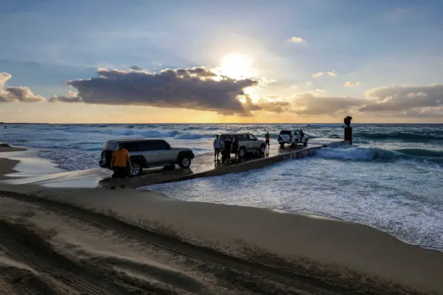 People stand by cars parcked along a concrete pier near sunset in al-Sabri district of Libya's eastern city of Benghazi on April 19, 2022