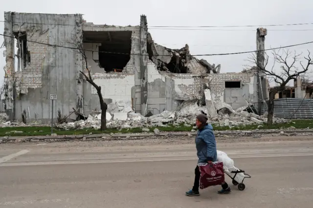 A local resident with bags walks past a destroyed in Mariupol