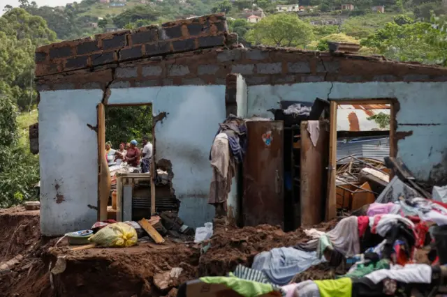 Neighbours stand next to the remains of a house at KwaNdengezi township outside Durban on April 15, 2022 where ten people are reportedly missing after their homes were swept away following the devastating rains and flooding.