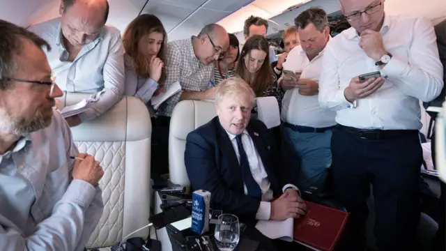 Boris Johnson surrounded by journalists on his flight to India