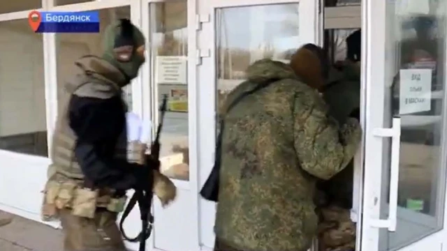 A screenshot from a Russian TV report showing armed men in military clothing entering the television station