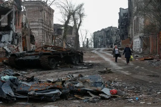 People walk near a destroyed tank and damaged buildings in the southern port city of Mariupol, Ukraine, on 22 April 2022