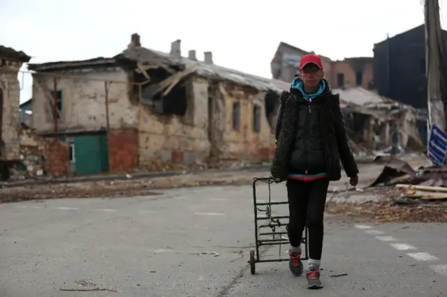 A woman with a trolley walks past ruined buildings in Mariupol