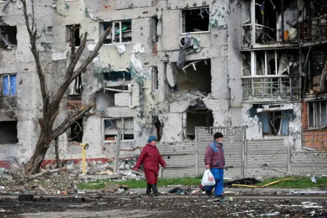 People walk near a destroyed residential building in Mariupol