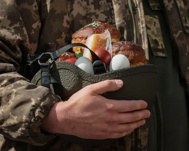 A Ukrainian serviceman holds an Easter cake and eggs in a helmet in Kyiv. Photo: 24 April 2022