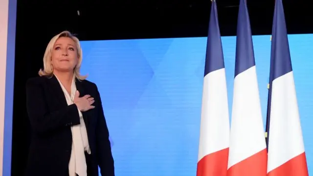 Marine Le Pen in front of three French flags