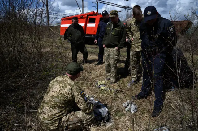 Officials look at shards of twisted metal from a Russian rocket in undergrowth near a train line on April 25, 2022 near Lviv, Ukraine.