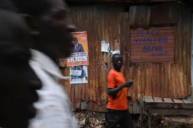 People walk past graffiti by a local artist on a residence, calling for peace during elections, on their way to nearby a polling station in Nairobi's Kibra slum,