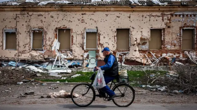 A cyclist bikes by a pockmarked building