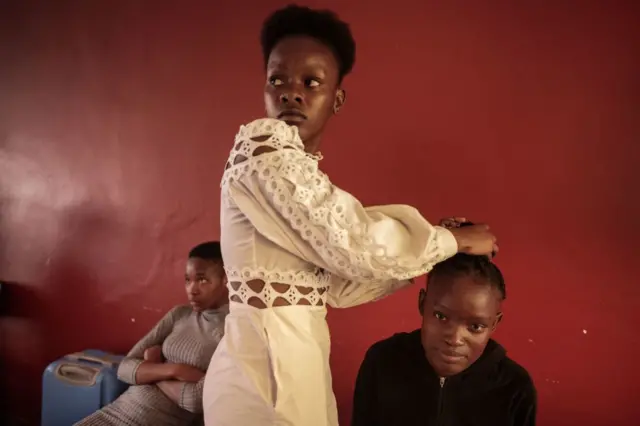 A girl (R) sits in the backstage of Miss Freedom Day in Bapedi Community All in Soweto as her sister (C) styles her hair before the exhibition, on April 27, 2022