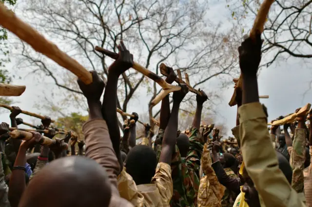 Trainee soldiers for a new unified army raise their wooden rifles at a makeshift barracks in Mapel, South Sudan - January 2020