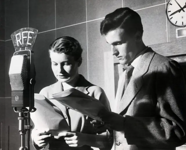 A man and a woman read into a microphone