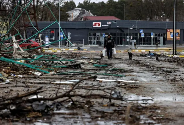 Image shows man walking with food bags in Bucha around rubble