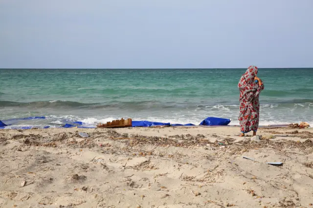 A Libyan woman stands next to the remains of a dingey and life jackets that washed up on the beach after dozens of migrants drowned in a shipwreck off the coast of Sabrata