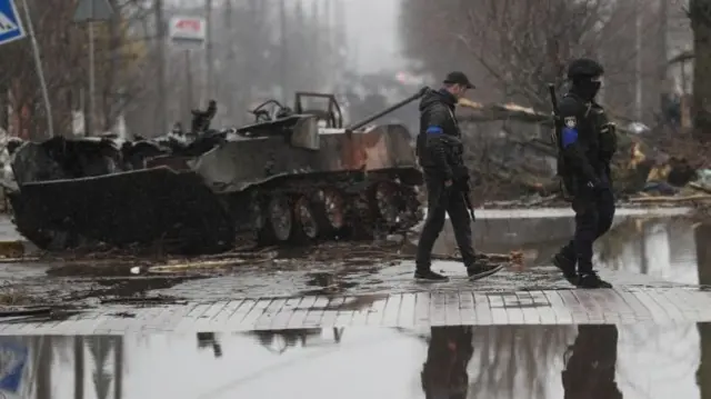 Ukrainian on patrol near a destroyed Russian tank