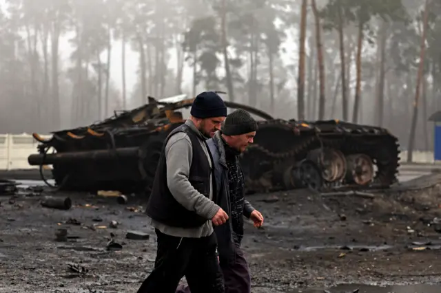 Locals walk past a destroyed Russian tank in the village of Dmytrivka, on the western outskirts of Kyiv, 1 April 2022