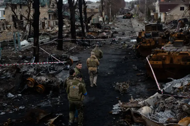 Ukrainian servicemen walk on the destroyed street in Bucha