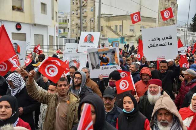 Tunisian protesters raise placards and national flags during a demonstration against their president,