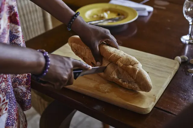 A woman cuts bread on a board.