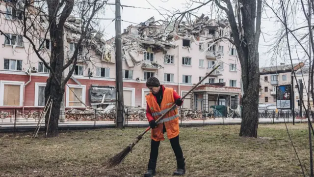 A person cleans in front of a destroyed building in Chernihiv