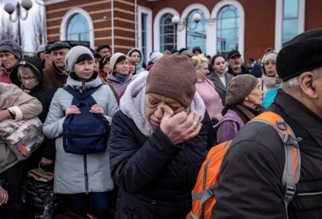 A woman wipes her eye as families wait to board a train as they flee the eastern city of Kramatorsk