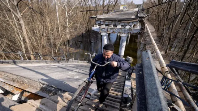 A man crosses a destroyed bridge with a bicycle