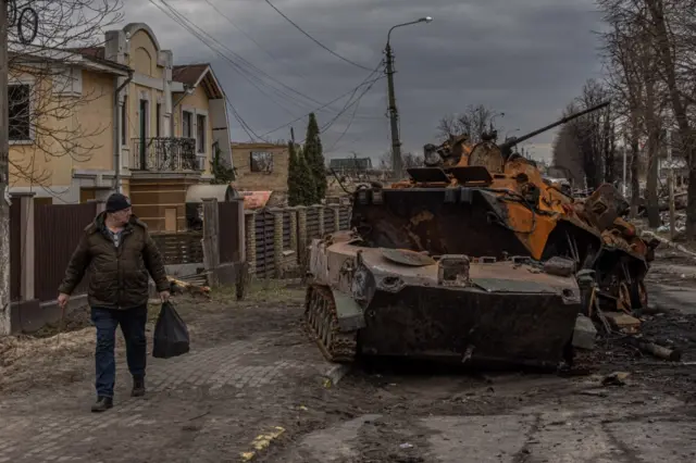 A resident of Bucha walks past destroyed Russian military equipment