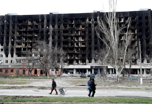 Local residents walk past a burned building in the southern port city of Mariupol