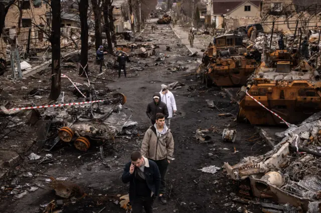 People walk through debris on a street in Bucha, following the withdrawal of Russian forces