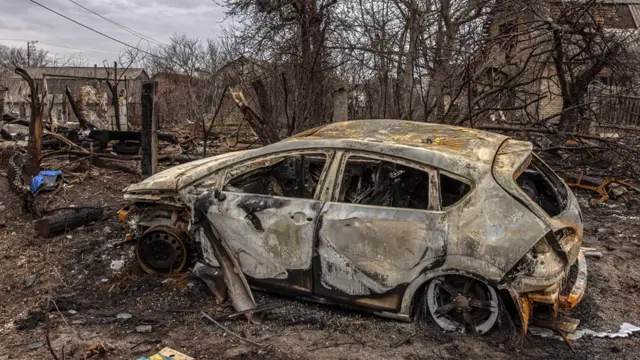 A burned car next to destroyed houses, in Bucha,