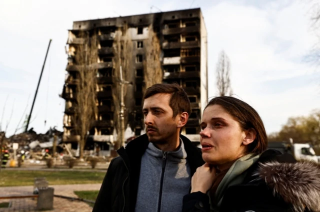 Serhii Prudyus and his wife Yulia in front of a bombed building in Borodyanka