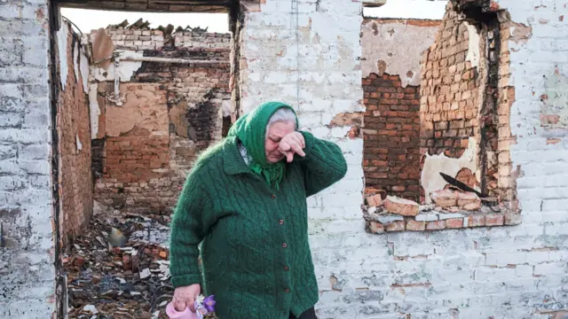 An elderly woman walks through her destroyed house in the village of Andriivka, near Kyiv