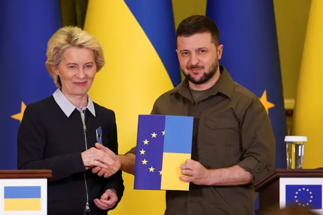 European Commission President Ursula von der Leyen shaking hands with Ukrainian President Volodymyr Zelensky and smiling at camera