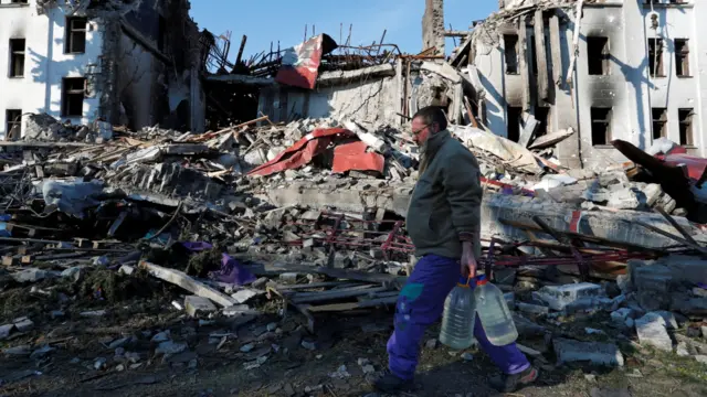 A man carries bottles of water past a destroyed theatre in Mariupol