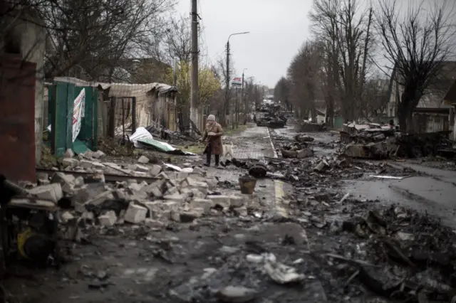 An elder woman walks amid destruction on a street in the town of Bucha, on the outskirts of Kyiv, after the Ukrainian army secured the area following the withdrawal of the Russian army