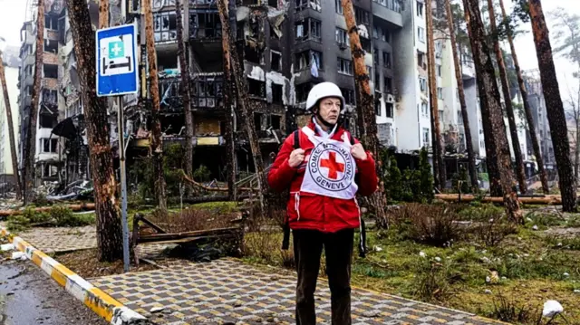 A Red Cross member stands in front of a destroyed building in Irpin