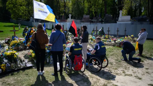 People, including two athletes in wheelchairs, gather at a grave in Lviv