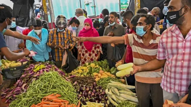 A crowd of people gather around a pile of food in Sri Lanka