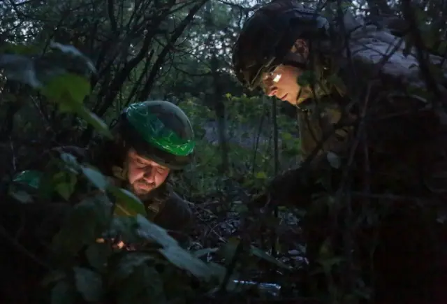 Two Ukrainian soldiers pictured sheltering in bushes at dusk