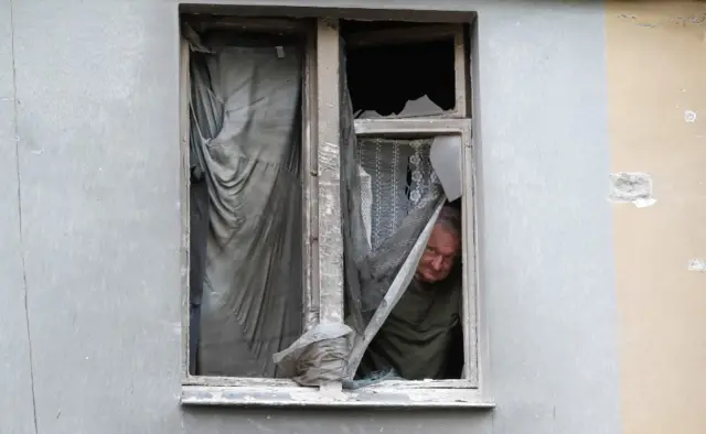 A Mariupol resident peers out of a shattered window