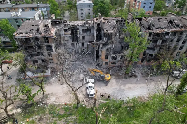 Drone footage shows a digger excavating rubble from a shattered housing block